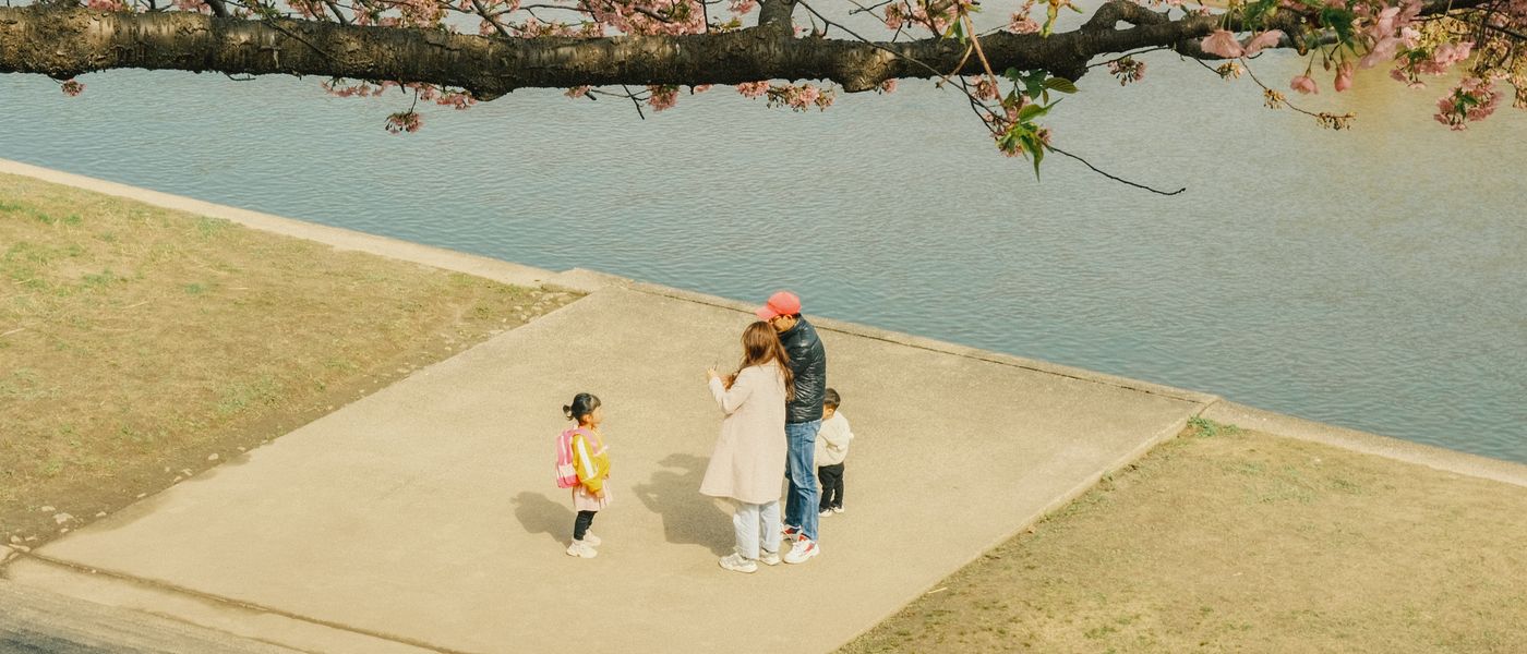 桜の咲く川辺で過ごす家族(イメージ)